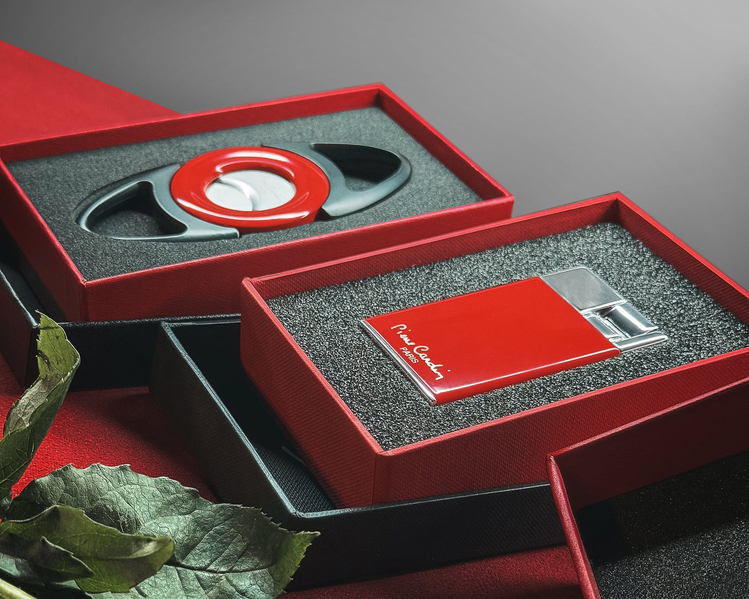 Cigar cutter and lighter set in a red and black box with a rose on a red surface.